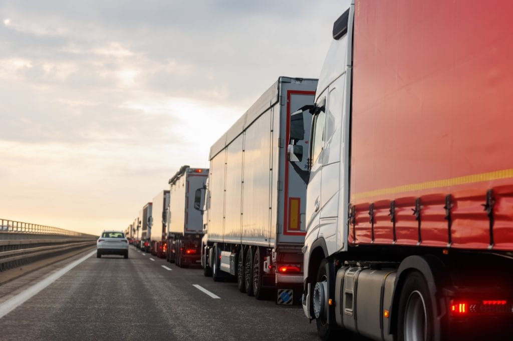 Line of articulated lorries and trucks stuck in traffic on a motorway at dusk, illustrating the limitations of traditional road freight transport compared to drone solutions.