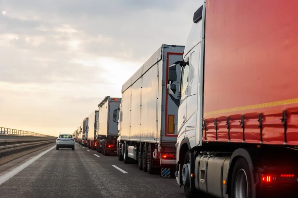 Line of articulated lorries and trucks stuck in traffic on a motorway at dusk, illustrating the limitations of traditional road freight transport compared to drone solutions.