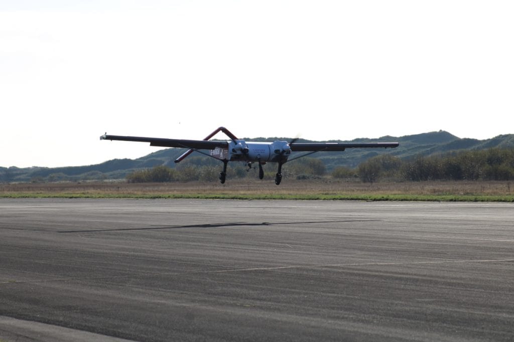 Windracers ULTRA autonomous drone with twin propellers coming in to land on a runway, with grassy hills and clear skies in the background.