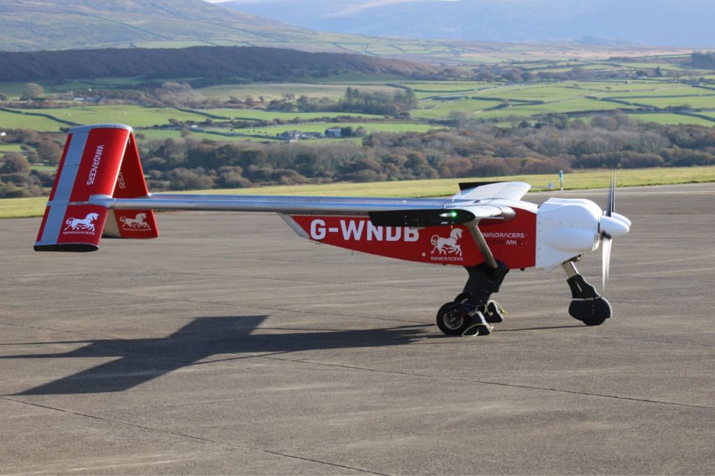 Autonomous delivery drones: Red and white fixed-wing cargo drone parked on runway with countryside backdrop.