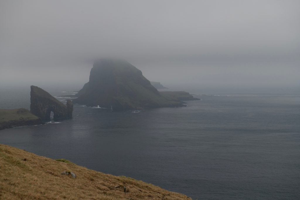 Cargo drones for mail: Rugged rocky island coastline shrouded in mist above the sea.