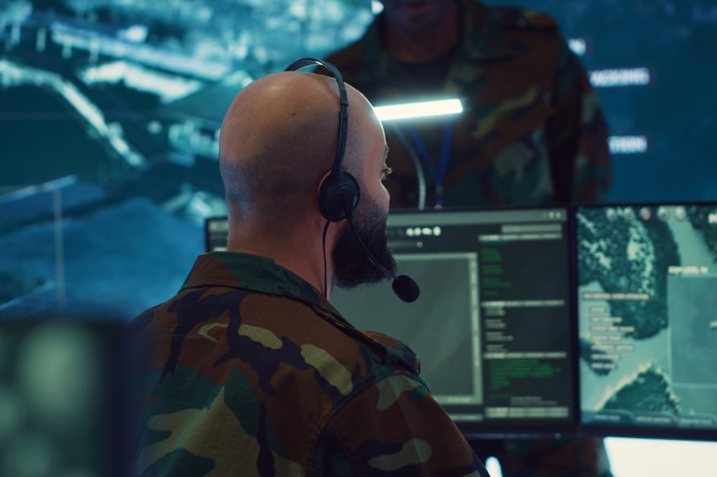Defence logistics drone: Military operator wearing headset monitoring drone systems on multiple screens.
